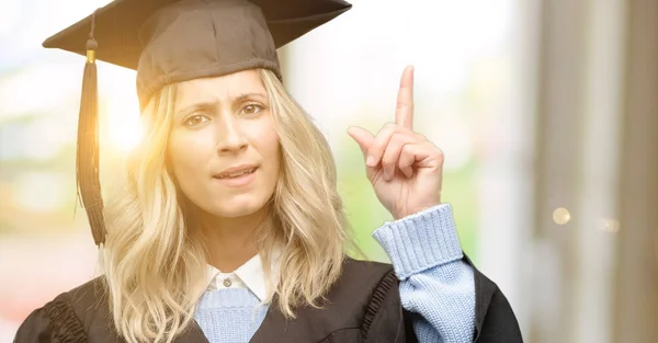 Young graduate woman happy and surprised cheering expressing wow gesture pointing up