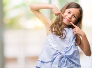 Esmer Latin kız kendinden emin gösterilen ve işaret parmakları diş ve ağız ile gülümseyen. Sağlık kavramı.