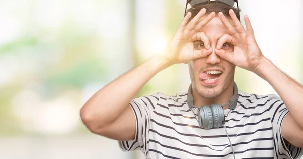 Handsome Young Man Wearing Headphones Doing Gesture Binoculars Sticking Tongue — Stock Photo, Image