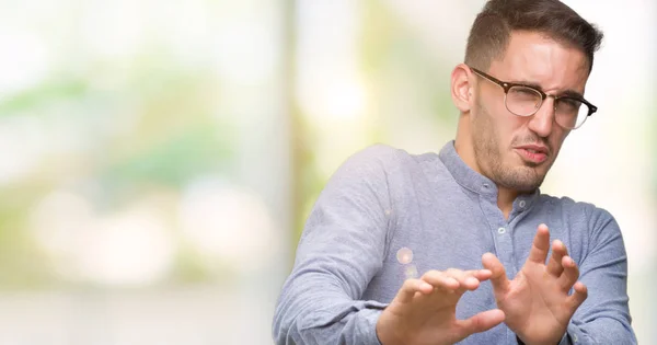 Handsome young elegant man wearing glasses disgusted expression, displeased and fearful doing disgust face because aversion reaction. With hands raised. Annoying concept.