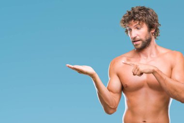 Yakışıklı İspanyol modeli adam seksi ve gömleksiz üzerinden hayran ve el ile sunulması ve parmak ile işaret ederken kameraya gülümseyen izole arka plan.