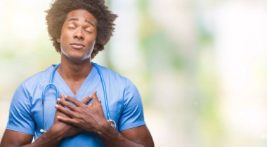 Afro Amerikalı cerrah doktor adam kapalı gözler ile göğüs ellerinde ve yüzünde minnettar jest ile gülümseyen izole arka plan. Sağlık kavramı.