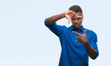 Afrikalı-Amerikalı genç elle yapma çerçeve ve parmakları ile mutlu yüz gülümseyen izole arka plan üzerinde. Yaratıcılık ve Fotoğrafçılık kavramı.