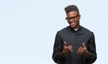 İzole arka plan başarı işareti el ile olumlu hareketi yaparken genç Afro-Amerikan rahip adam başparmak gülümseyen ve mutlu. Neşeli bir ifadeyle, kazanan jest kameraya bakıyor.