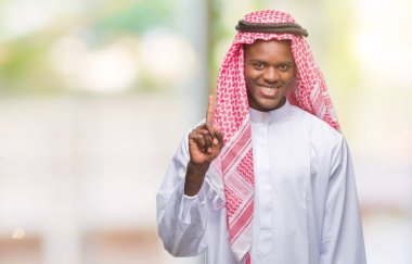 Geleneksel keffiyeh ve parmak gülümseyen süre bir numara ile kendinden emin ve mutlu yukarıyı gösteren izole arka plan üzerinde giyen genç Arapça Afrika adam.