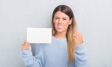 Gri grunge duvar holding boş kartı rahatsız Genç Yetişkin kadın ve boşa çıkarmak ile öfke, çılgın ve yükseltilmiş eliyle diye bağıran öfke kavramı bağırarak.