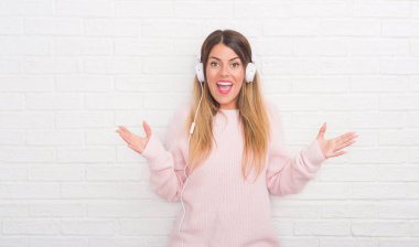 Müzik ve dans çok mutlu ve heyecanlı, kazanan ifade büyük gülümseme ile çığlık zaferini kutluyor kulaklıklar giyen ve ellerini kaldırdı beyaz tuğla duvarın üzerinden Genç Yetişkin kadın