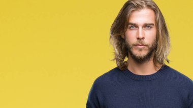 Genç yakışıklı adam uzun saçlı yüzünde ciddi bir ifade ile izole arka plan üzerinde kış kazak giyiyor. Basit ve doğal kameraya bakıyor.