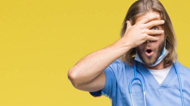 Yüz ve gözler el ile kapsayan şok izole arka plan bakmak üzerinde uzun saçlı Genç yakışıklı Doktor adam utanç ifadesi ile parmaklarımın arasından bakan.
