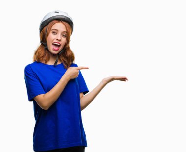 Hayret ve el ile sunulması ve parmak ile işaret ederken kameraya gülümseyen izole arka plan üzerinde bisikletçi kask giyen genç güzel kadın.