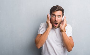 Yakışıklı genç bir sürpriz yüz, korkuyor ve heyecanlı korku ifadesi ile şok korkmuş müzik dinlerken kulaklık giyen gri grunge duvarın üzerinden