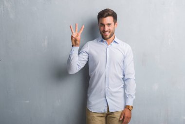 Yakışıklı genç iş adamı gösterilen ve parmakları ile işaret şık gömlek giymiş gri grunge duvarın üzerinden üçüncü ise kendinden emin ve mutlu gülümseyerek.