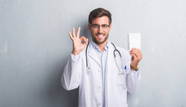 Parmak, mükemmel sembolü ile ok işareti yapıyor boş defter tutan gri grunge duvarın üzerinden adam yakışıklı genç doktor