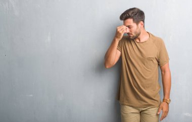 Yakışıklı genç gri grunge duvar yorgun sürtünme burun ve göz yorgunluğu ve baş ağrısı hissediyor. Stres ve hayal kırıklığı kavramı.