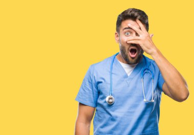 Mahcup ifadeyle parmaklarımın arasından görünen yüz ve gözler el ile kapsayan şok izole arka plan bakmak üzerinde genç yakışıklı Doktor cerrah adam.