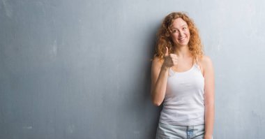 Gri grunge duvar ok işareti, başparmak ile parmak, mükemmel işareti yapıyor kocaman bir gülümseme ile mutlu genç Kızıl saçlı kadın