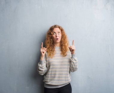 Genç Kızıl saçlı kadın gri grunge duvarın üzerinden hayran ve yukarıya bakıp parmakları ile işaret şaşırttı ve silah kaldırdı.