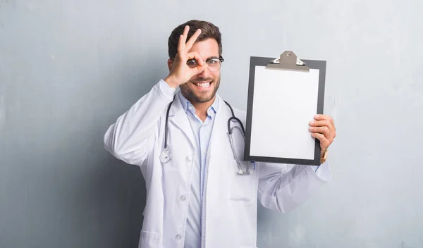 Handsome Young Doctor Man Grey Grunge Wall Holding Clipboard Happy — Stock Photo, Image