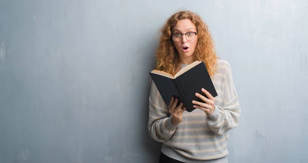 Joven Pelirroja Sobre Pared Grunge Gris Leyendo Libro Asustada Shock — Foto de Stock