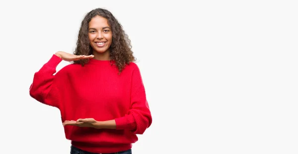 メジャー シンボル兆し大きな 大きなサイズの手で身振りで示す赤いセーターを着ている若いヒスパニックの女性 カメラを見て笑っています 測定概念 — ストック写真