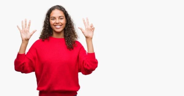 年轻的西班牙裔妇女穿着红色毛衣显示和指向手指八 而微笑着自信和快乐 — 图库照片
