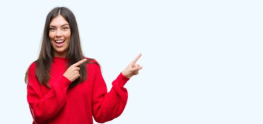 Genç güzel İspanyol giyen kırmızı kazaklı gülümseyen ve iki elleri ve parmakları ile tarafına işaret kamera bakıyor.