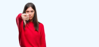 Genç güzel İspanyol mutsuz ve kızgın ret gösterilen ve başparmak aşağı hareketi ile negatif seyir kırmızı kazak giyiyor. Kötü ifade.