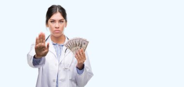 Açık eliyle dur işareti ile ciddi ve kendine güvenen ifade, savunma jest yapıyor dolar tutan genç İspanyol doktor kadın