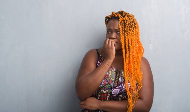 Gri grunge duvar turuncu örgü stresli ve gergin elle çivi ısırma ağzına bakarak giyen genç Afro-Amerikan kadın. Anksiyete sorunu.