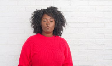 Genç Afro-Amerikan artı boyutu kadın beyaz tuğla üzerinden dudaklı, çılgın ve komik bir jest yapma balık yüz duvar. Komik ifade.