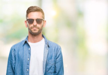 Genç yakışıklı adam yüzünde ciddi bir ifade ile izole arka plan üzerinde güneş gözlüğü takıyor. Basit ve doğal kameraya bakıyor.