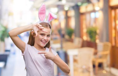 Paskalya bunny kulaklar elle yapma çerçeve ve parmakları ile mutlu yüz gülümseyen izole arka plan üzerinde giyen genç güzel kız. Yaratıcılık ve Fotoğrafçılık kavramı.