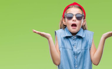 Genç güzel kız izole arka plan clueless ve şaşkın bir ifadeyle kollar ve eller kaldırdı üzerinde güneş gözlüğü takıyor. Şüphe kavramı.