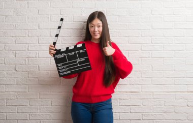 Ok işareti, başparmak ile parmak, mükemmel işareti yapıyor kocaman bir gülümseme ile fıçı tahtası mutlu holding beyaz tuğla duvarın üzerinden Genç Çinli kadın