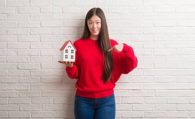 Genç Çinli gerçek durum Aracısı kadın kendisine sürpriz yüz işaret parmağı ile ev tutan tuğla duvarın üzerinden