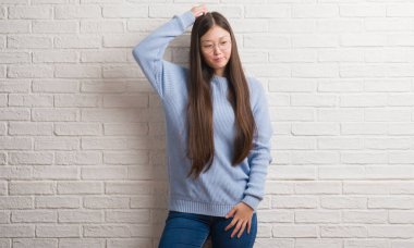 Genç Chinise kadın beyaz tuğla duvarın üzerinden yanıltır ve soru hakkında merak ediyorum. Şüphe, kafasına el ile düşünme ile belirsiz. Dalgın kavramı.