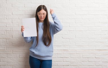 Tuğla Genç Çinli kadın boş kağıt rahatsız tutarak ve öfke, deli ile sinirli bağırarak duvar ve yükseltilmiş el ile bağırmaya kavramı öfke