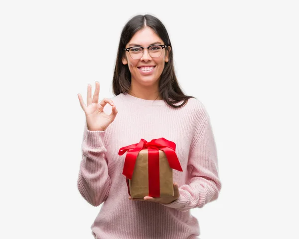 Joven Mujer Hispana Sosteniendo Regalo Haciendo Signo Con Los Dedos — Foto de Stock