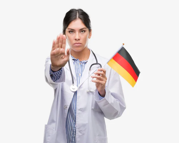年轻西班牙裔医生妇女持有德国国旗与张开手做停止标志认真和自信的表达 防御姿态 — 图库照片