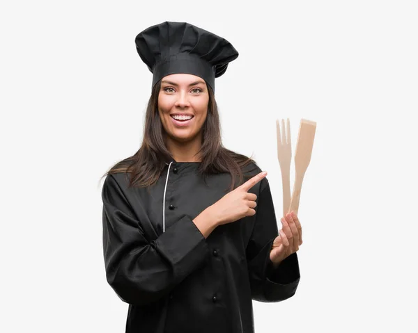 年轻的西班牙裔厨师妇女穿着厨师制服很高兴指着手和手指的侧面 — 图库照片