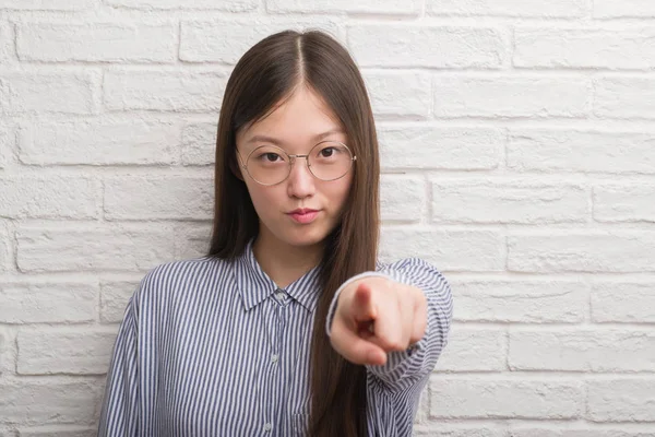 年轻的中国企业妇女在砖墙指向照相机和对您 手标志 正面和自信手势从前面 — 图库照片