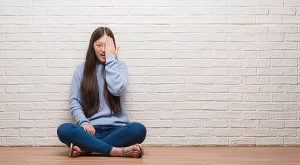 一位年轻的中国女子坐在砖墙上 脸上充满自信的笑容和惊讶的情绪 用手捂住一只眼睛 — 图库照片