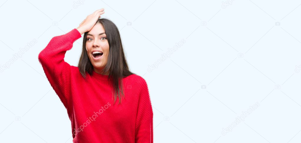 Young beautiful hispanic wearing red sweater surprised with hand on head for mistake, remember error. Forgot, bad memory concept.