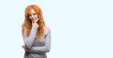 Çapraz kollar ve çeneme kaldırdı el ile gülümseme ile kameraya kendine güvenen arayan genç Kızıl saçlı kadın. Pozitif düşünce.