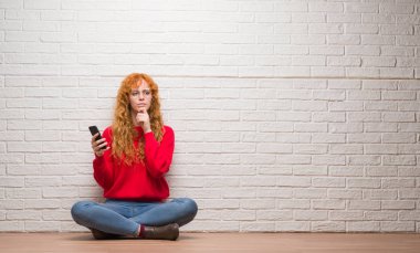 Tuğla duvar üzerine telefon ciddi bir yüz düşünme hakkında soru, çok karışık fikir söz üzerine oturan genç Kızıl saçlı kadın