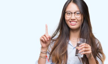 Genç Asyalı kadın izole arka bir fikir ya da soru işaret parmağı ile gülen yüz, sürpriz üzerine bir bardak su içme bir numara