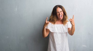 Deli ifade rock simge elle yapıyor ile gri grunge duvar bağırarak üzerinde duran orta yaş İspanyol kadın. Müzik yıldızı. Ağır kavramı.