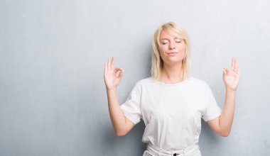 Yetişkin kafkas kadın grunge gri duvarın üzerinden rahatla ve gülümseyen gözlerle parmak ile meditasyon jest yapıyor kapalı. Yoga kavramı.