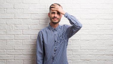 Genç yetişkin adam kafasına, utanç ve sürpriz yüz ile şok el ile vurguladı beyaz tuğla duvarın üzerinden ayakta öfkeli ve sinirli. Korku ve hata için üzgün.