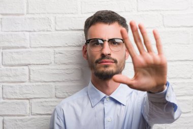 Genç Yetişkin iş adam beyaz tuğla duvarın üzerinden açık eliyle dur işareti ile ciddi ve kendine güvenen ifade, savunma jest yapıyor ayakta